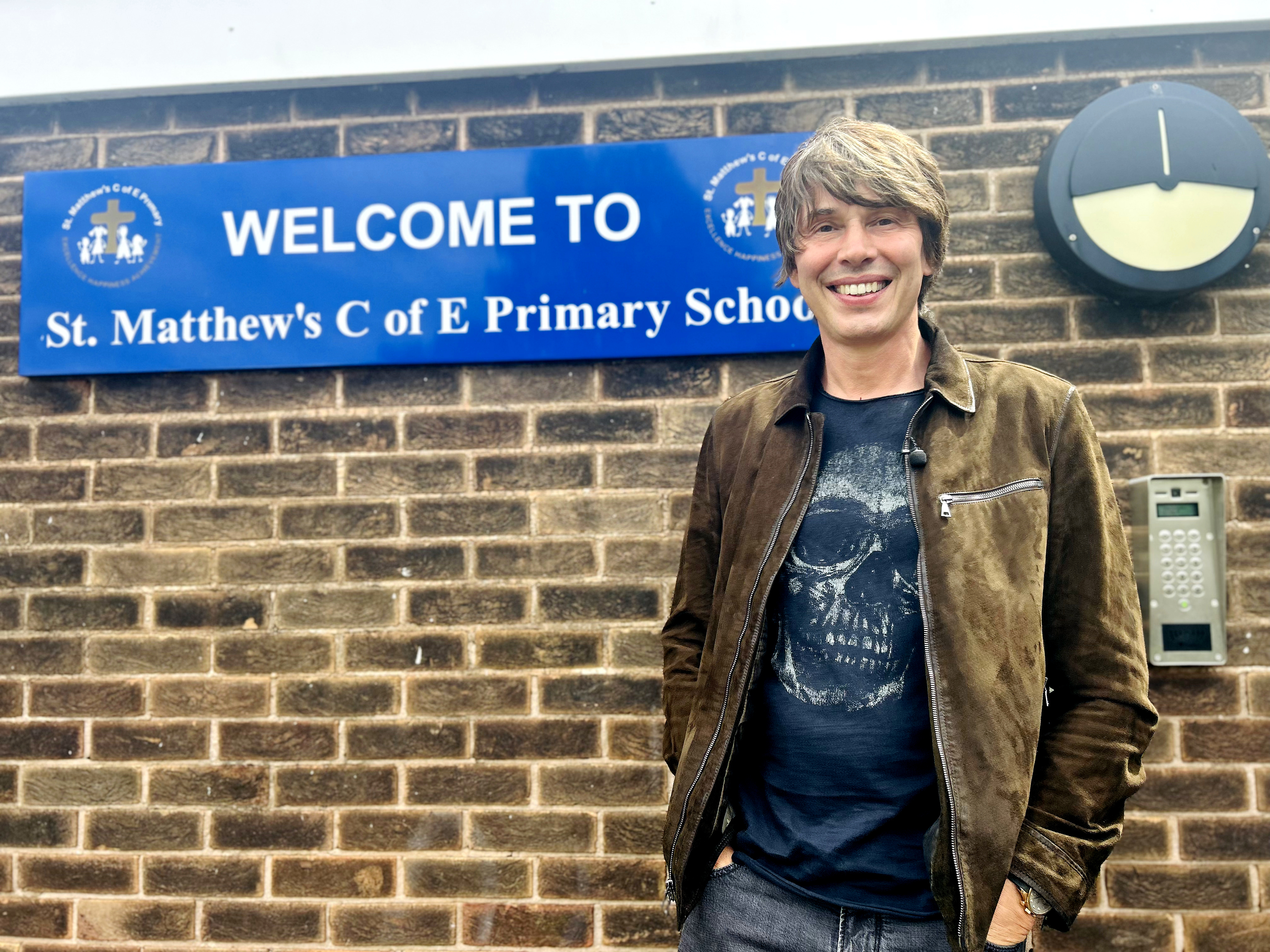 Professor Brian Cox smiling outside his old school St Matthew's in Chadderton