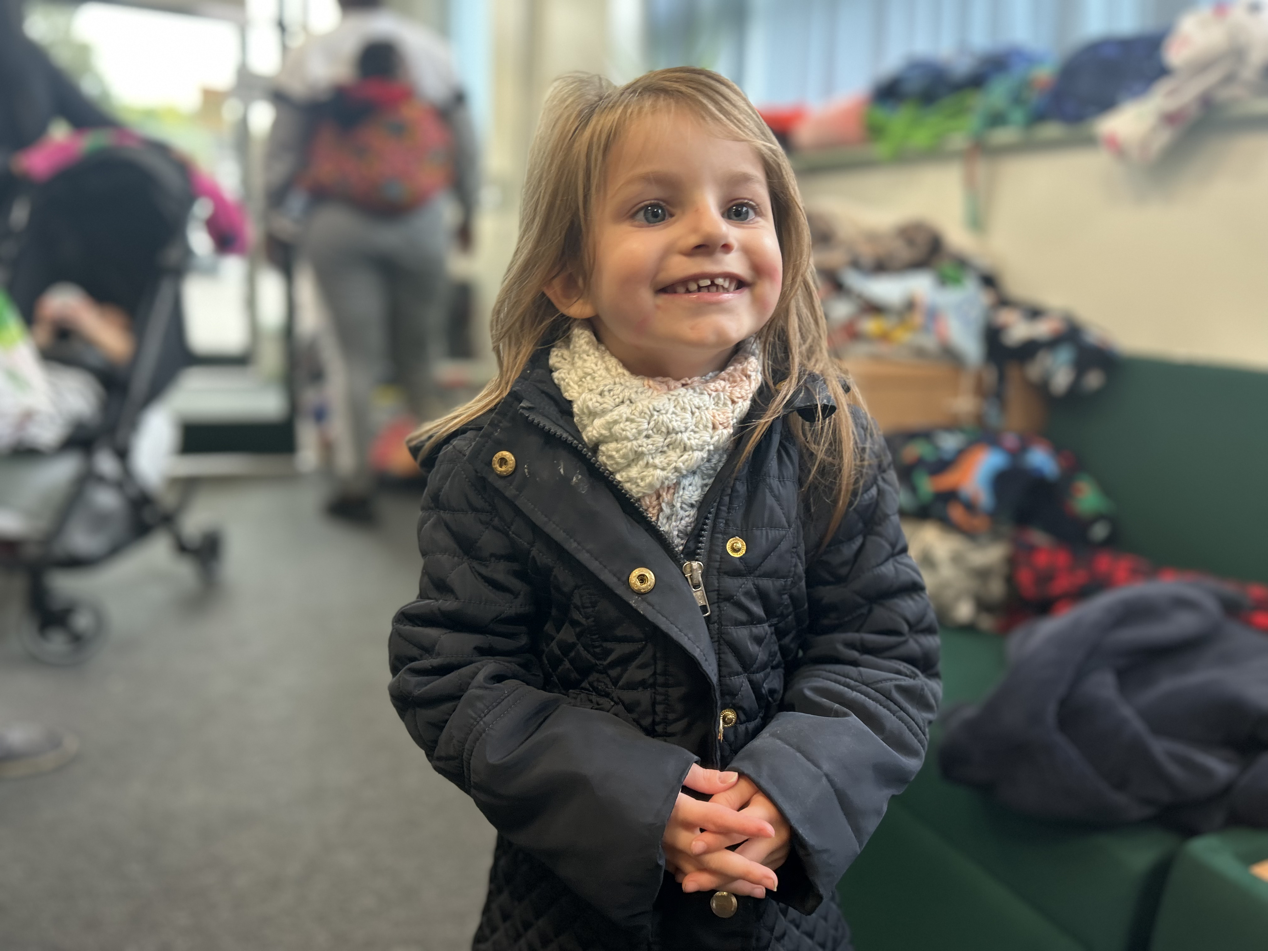 Three-year-old Isabella Rees smiling in a warm navy blue coat and woollen scarf at Spring Meadows Family Hub